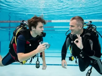 Tauchanfänger übt Angst vor Maskenabnahme mit einem ruhig begleitenden Tauchlehrer im Schwimmbad.
