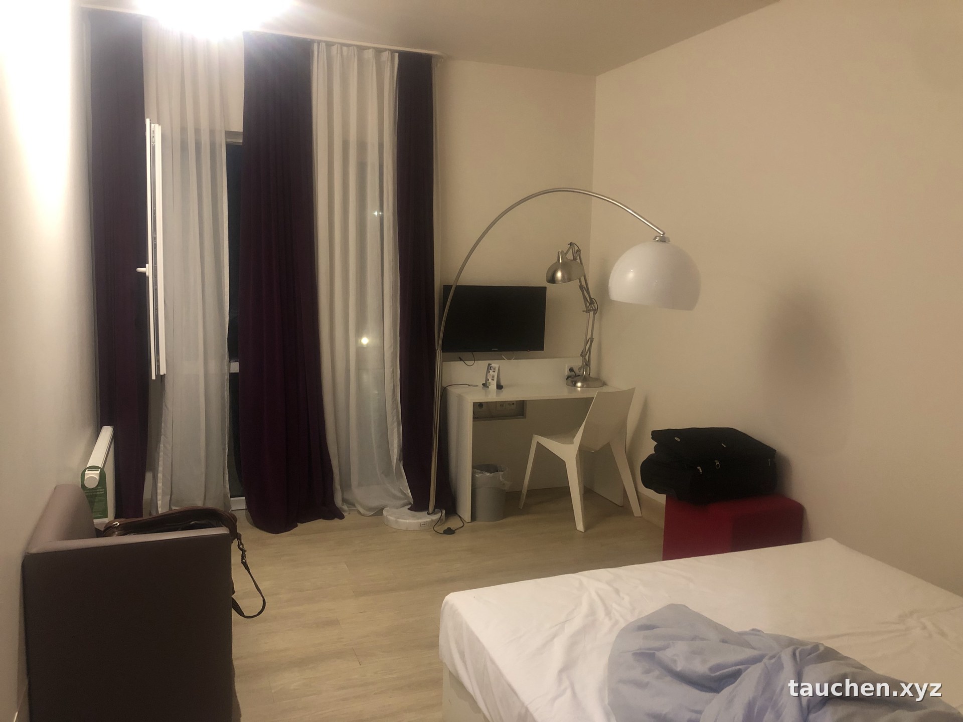 Hotelzimmer mit Doppelbett, Schreibtisch, Stehlampe und Fernseher