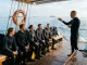 Ein Divemaster hält an Bord eines Tauchbootes das Briefing vor einer sitzenden Tauchergruppe.