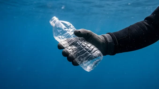Behandschuhte Taucherhand hält unter Wasser eine verschlossene Kunststoffflasche, die vom Umgebungsdruck sichtbar eingedellt ist.
