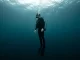 Vollständig ausgerüsteter Taucher sinkt mit entlüftetem Tarierjacket aufrecht und füße voran in tieferes Wasser ab.