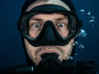 Nahaufnahme eines Tauchergesichts hinter der Maske mit starrem Blick und angespannter Gesichtsmuskulatur.