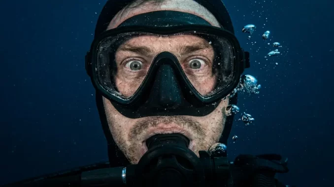 Nahaufnahme eines Tauchergesichts hinter der Maske mit starrem Blick und angespannter Gesichtsmuskulatur.