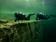 Zwei Taucher schwimmen in gleichbleibender Tiefe waagerecht an einer geraden Abbruchkante entlang.