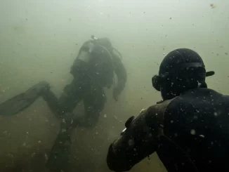 Taucher im truben Baggersee, der Tauchpartner ist in wenigen Metern Entfernung nur noch als Silhouette erkennbar.