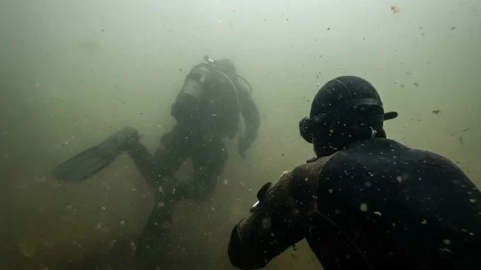 Taucher im truben Baggersee, der Tauchpartner ist in wenigen Metern Entfernung nur noch als Silhouette erkennbar.