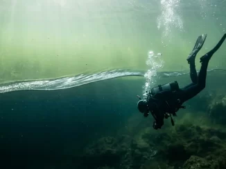 Taucher sinkt in einem See durch die flimmernde Sprungschicht, darunter wird das Wasser dunkler.