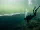 Taucher sinkt in einem See durch die flimmernde Sprungschicht, darunter wird das Wasser dunkler.