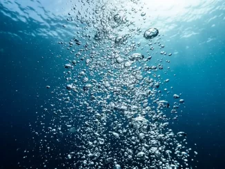 Aufsteigende Luftblasen im Gegenlicht vor tiefblauem Wasser.