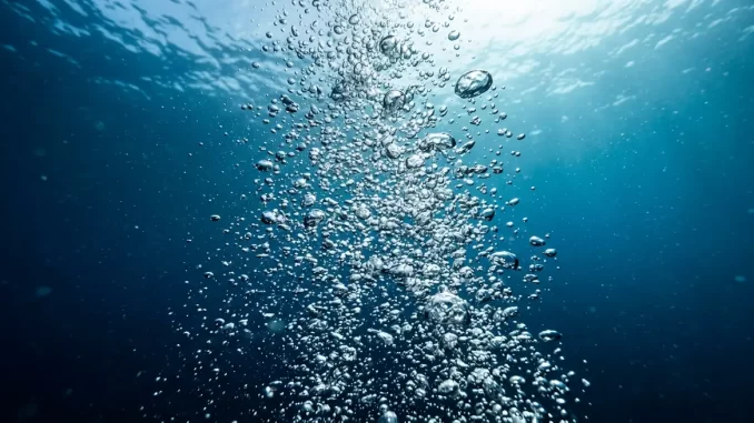 Aufsteigende Luftblasen im Gegenlicht vor tiefblauem Wasser.