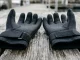 Ein Paar schwarze Neopren-Tauchhandschuhe mit genoppter Griffbeschichtung und Klettverschluss am Handgelenk liegt auf einem nassen Holzsteg.
