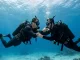 Zwei Taucher unter Wasser: Einer reicht dem anderen seinen Lungenautomaten zum Atmen.