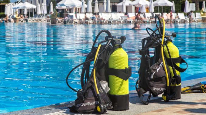 Zwei Tauchgerätesätze mit gelben Flaschen stehen am Beckenrand eines Freibads – typischer Aufbau für eine Tauchausbildung im Pool