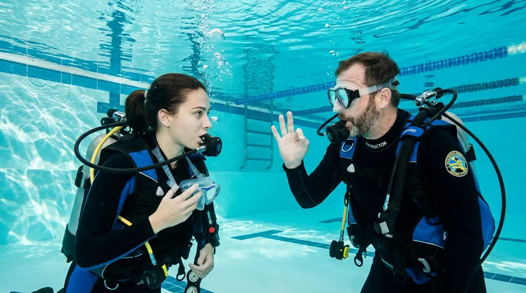 Tauchlehrer sichert einen Tauchanfänger bei der kontrollierten Maskenabnahme im Schwimmbad.