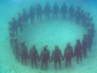 Kreis aus lebensgroßen Betonfiguren, die sich an den Händen halten, auf Sandgrund – die Unterwasserskulptur „Vicissitudes“ von Jason deCaires Taylor in Grenada