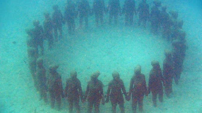 Kreis aus lebensgroßen Betonfiguren, die sich an den Händen halten, auf Sandgrund – die Unterwasserskulptur „Vicissitudes“ von Jason deCaires Taylor in Grenada