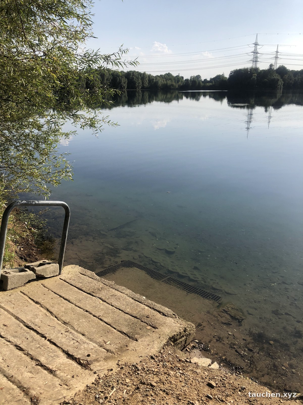 Befestigter Einstieg aus Betonplatten mit Metallgeländer am Seeufer, klares Flachwasser