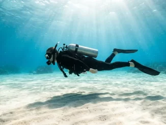 Taucher schwebt bewegungslos und waagerecht ueber hellem Sandgrund im hydrostatischen Gleichgewicht.
