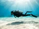 Taucher schwebt bewegungslos und waagerecht ueber hellem Sandgrund im hydrostatischen Gleichgewicht.