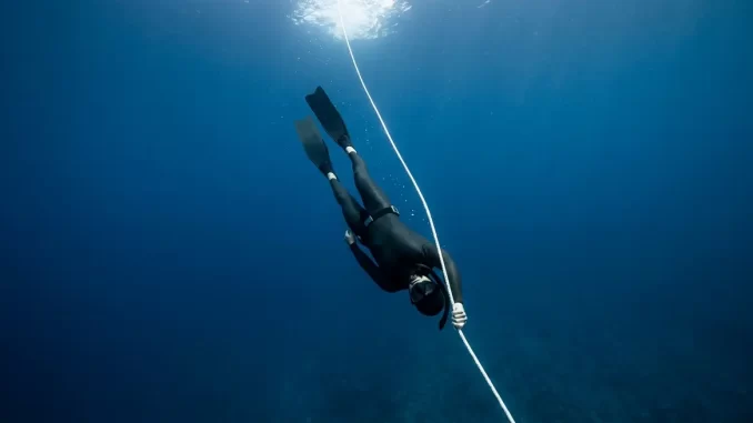 Apnoetaucher gleitet an einem senkrechten Abstiegsseil kopfüber ins tiefblaue Wasser hinab.