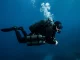Technischer Taucher mit Doppelgeraet und zwei seitlich angeclippten Stageflaschen in tiefblauem Wasser.
