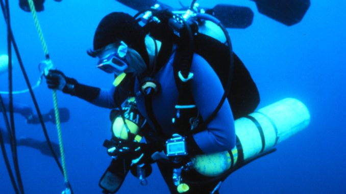 Technischer Taucher mit Doppelgerät, Stageflasche und Tauchcomputer hält sich beim Dekompressionsstopp an einer Leine im freien Wasser
